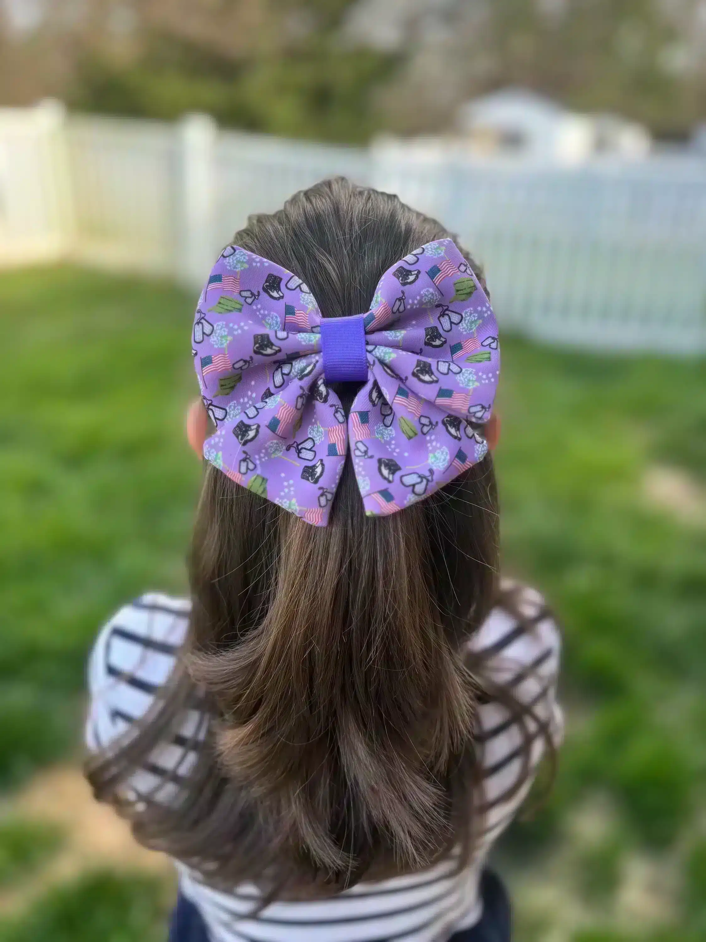 A girl wearing a large purple hair bow with dandelion and dog tag prints, showing the back of her head.