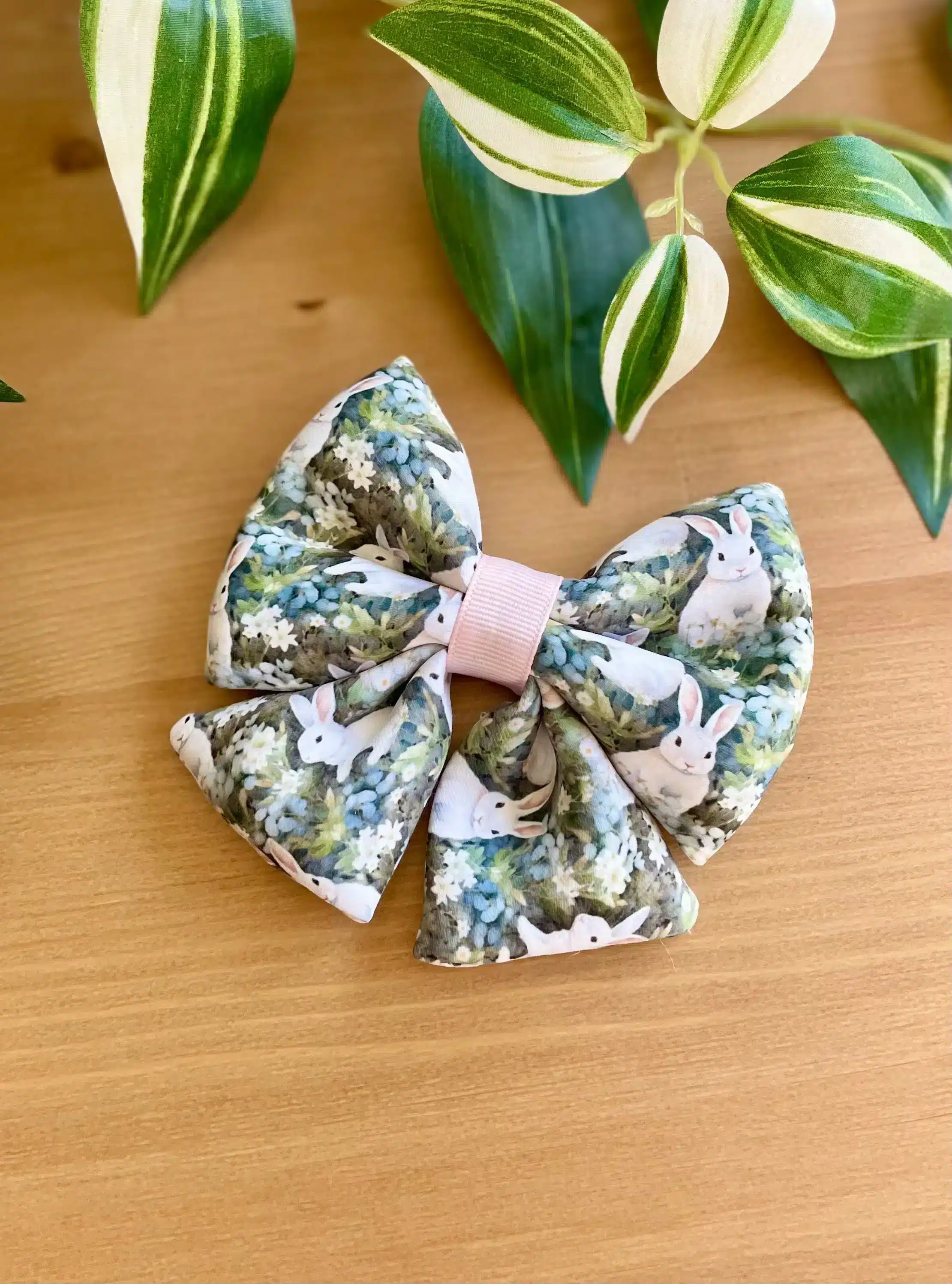 A handmade puffy hair bow with a cute bunny print, displayed on a wooden surface with green leaves in the background. The bow features a full, thick appearance, making it a standout accessory for girls and women.