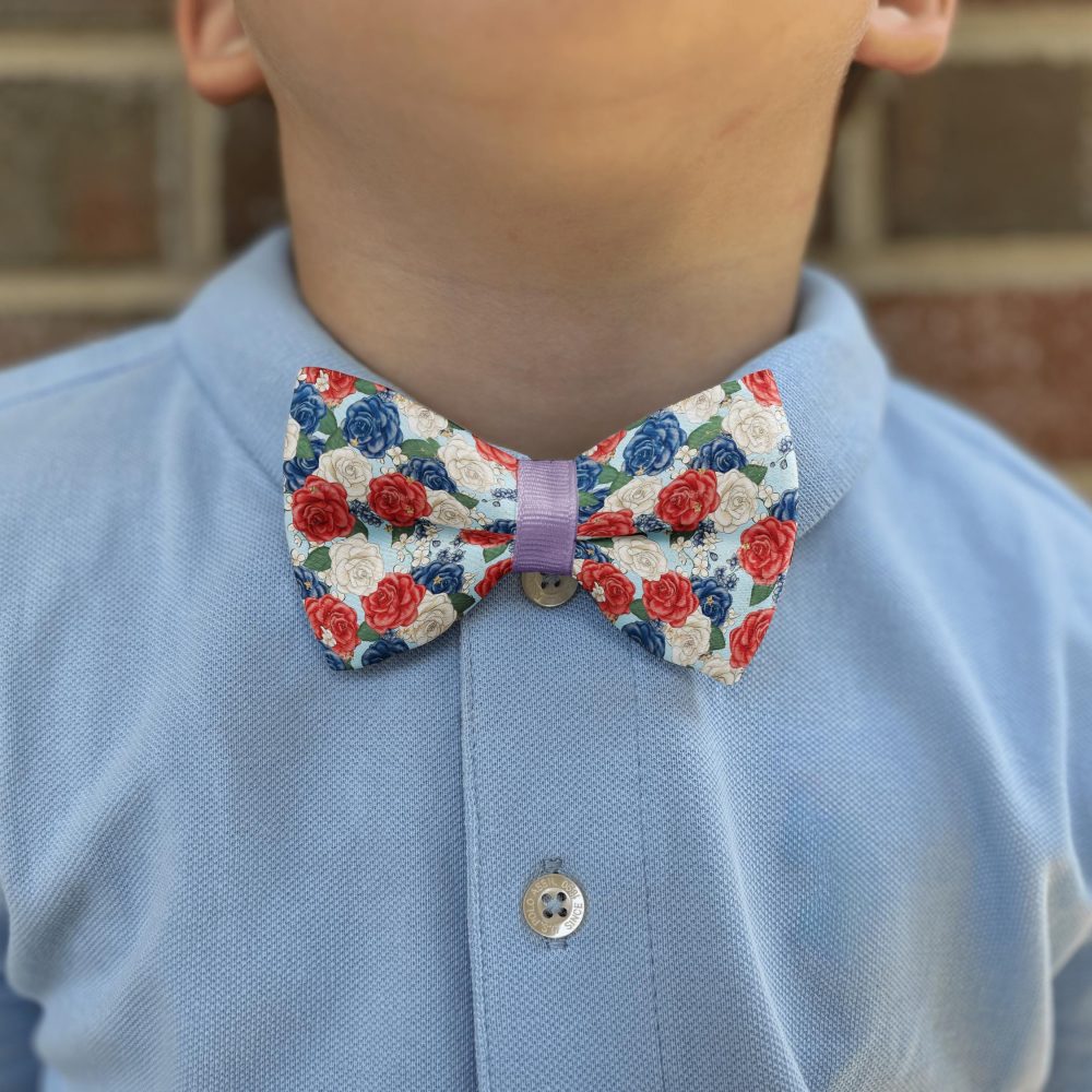 Child wearing floral bow tie with blue shirt.